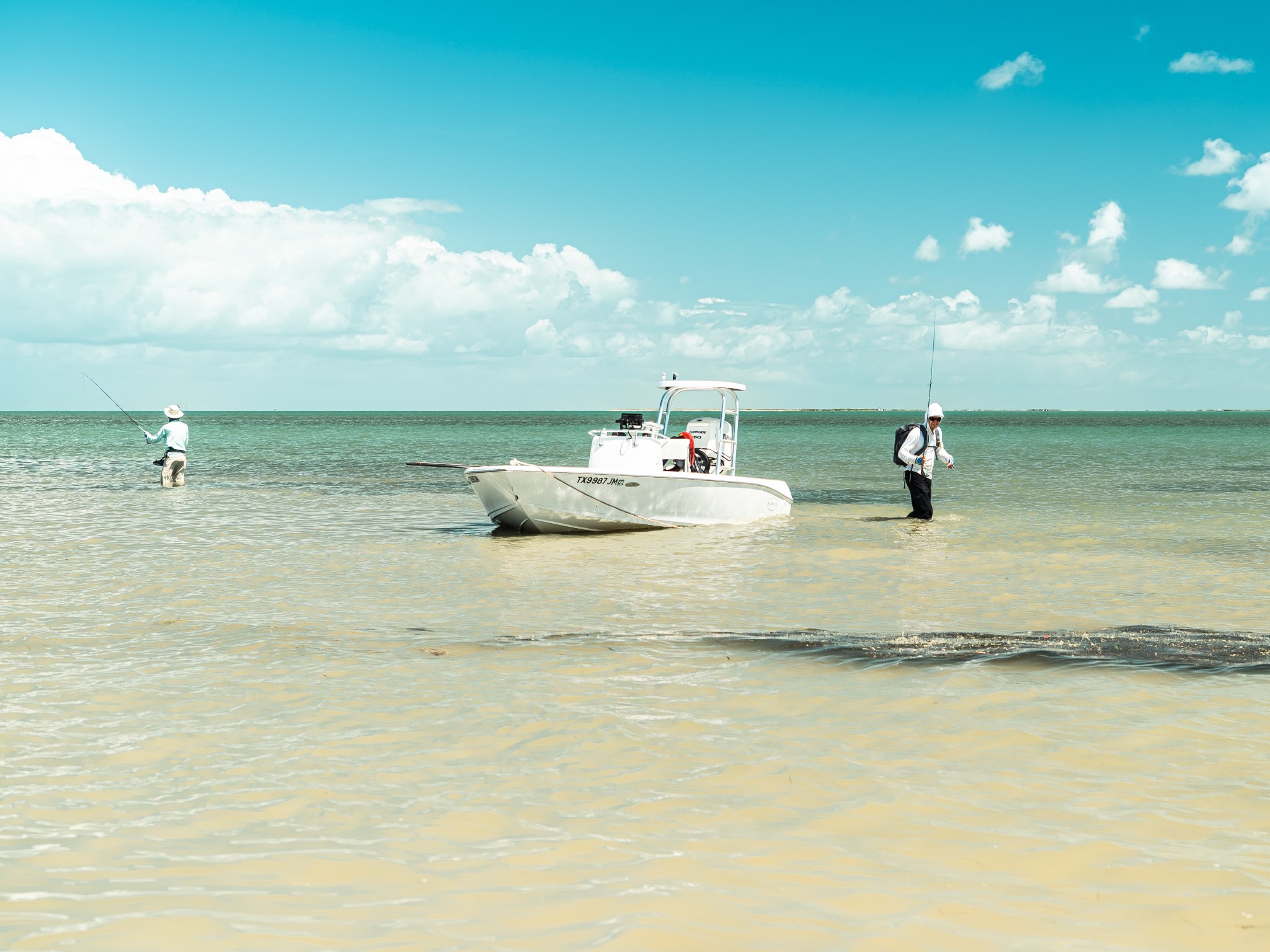 Two anglers wade-fishing the shallow Texas coastal flats beside a small white boat