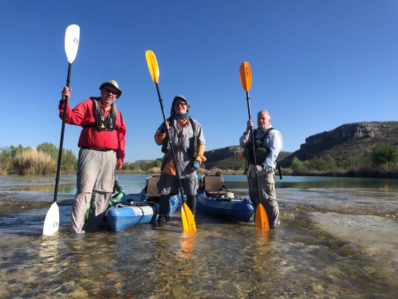 Three club members with kayaks and raised paddles on the Devils River