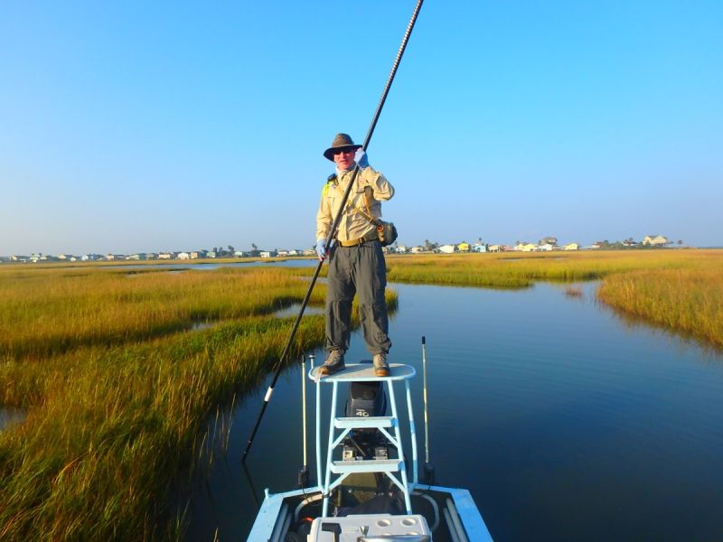 An angler poling a skiff through golden marsh grass at Bolivar