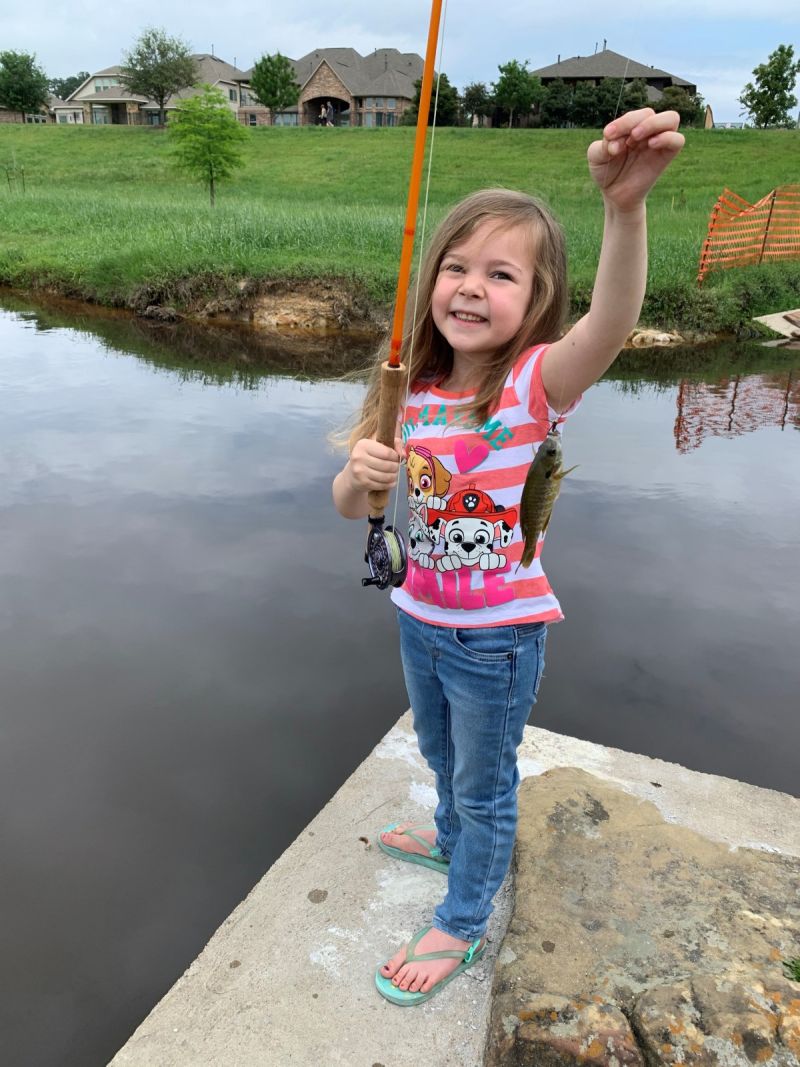 A smiling young girl holding up a fish she caught from a pond